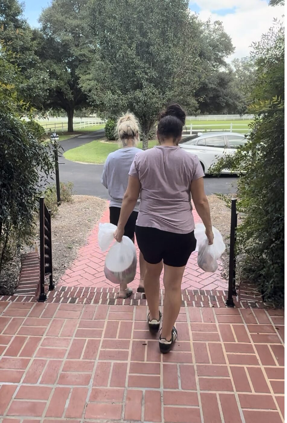 Angela and a Fresh Start team member carrying cleaning supplies down a walkway after finishing a job.
