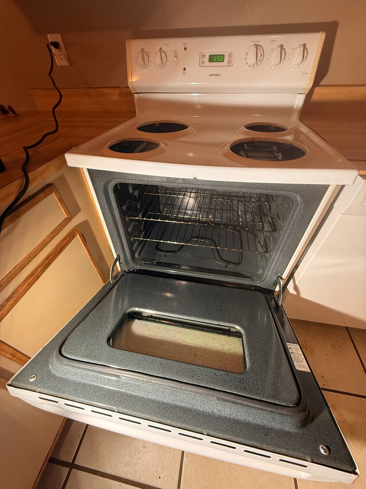 An empty oven with the door open and cabinet drawers pulled out in a vacant home during a move-out cleaning.