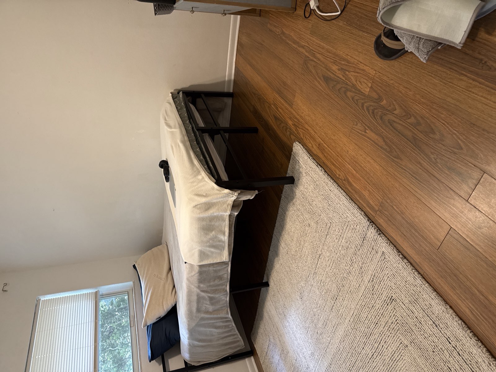 A tidy, move-in-ready bedroom with a made bed, clean wood flooring, and an area rug in a student apartment.